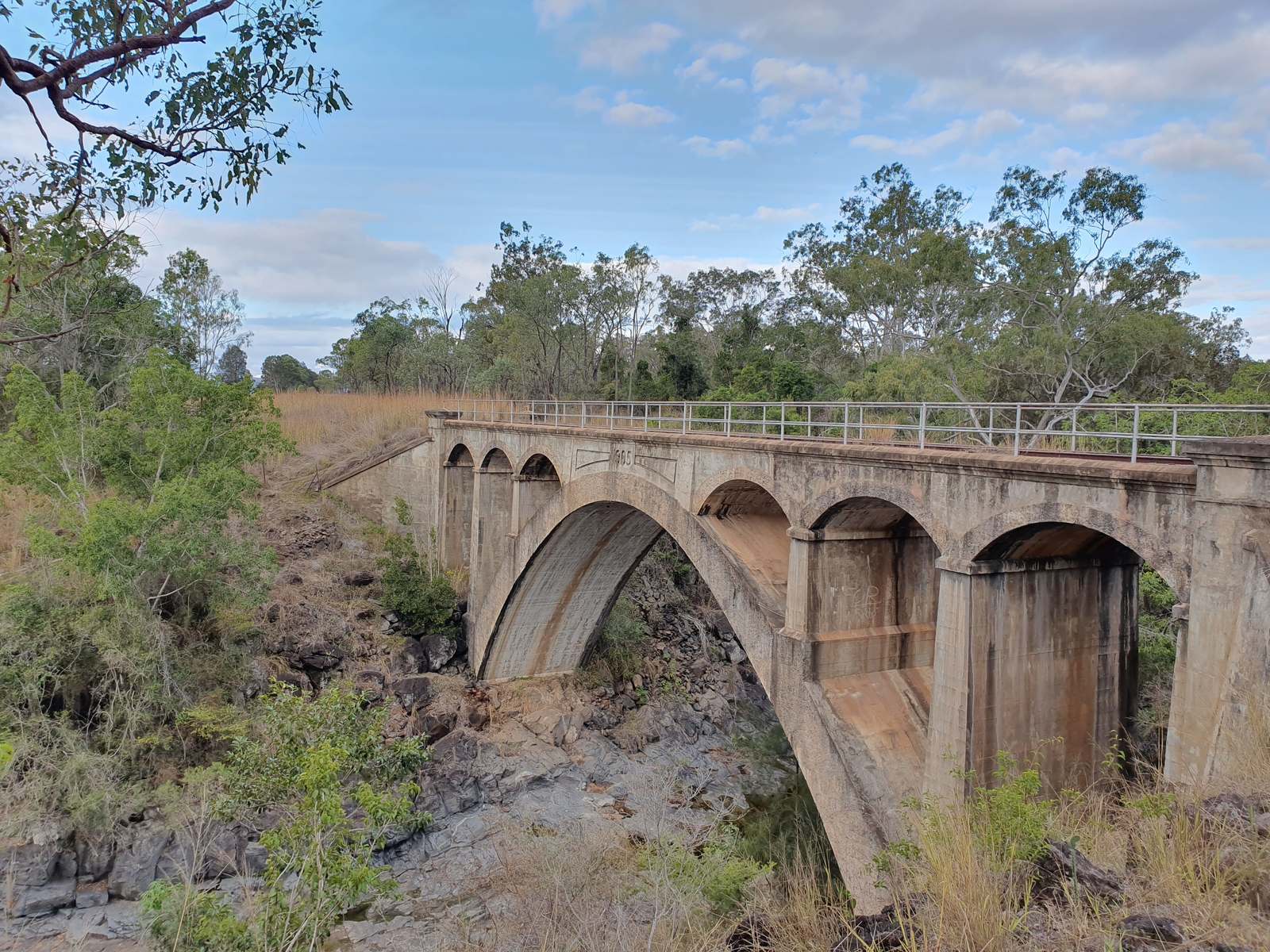 Heritage concrete arch rail bridge over a rocky creek in open eucalypt country, North Burnett, Queensland